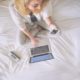 Frau mit Smartphone und Laptop sitzt auf Bett