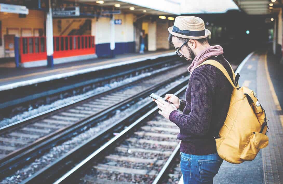 Mann mit Smartphone an Bahngleis